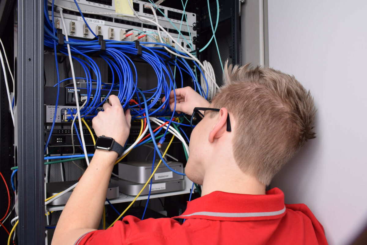 Blick über die Schulter eines Technikers, der blaue Kabel an einen Server anschließt